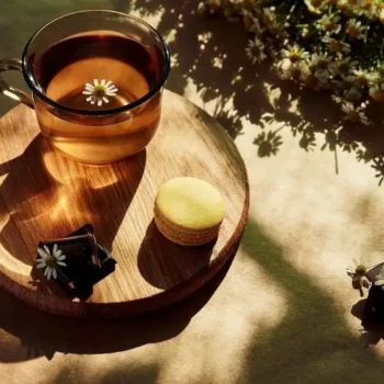 Golden hour of a tea cup, macaron, and chocolate with daisies on a table